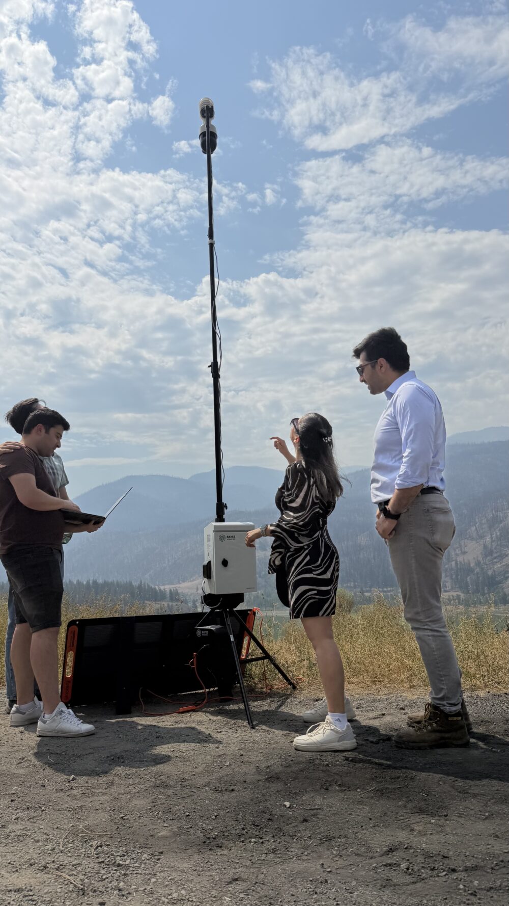 The Bayes Studio team stands on a hillside in Interior British Columbia, demonstrating their stationary multimodal monitoring unit.