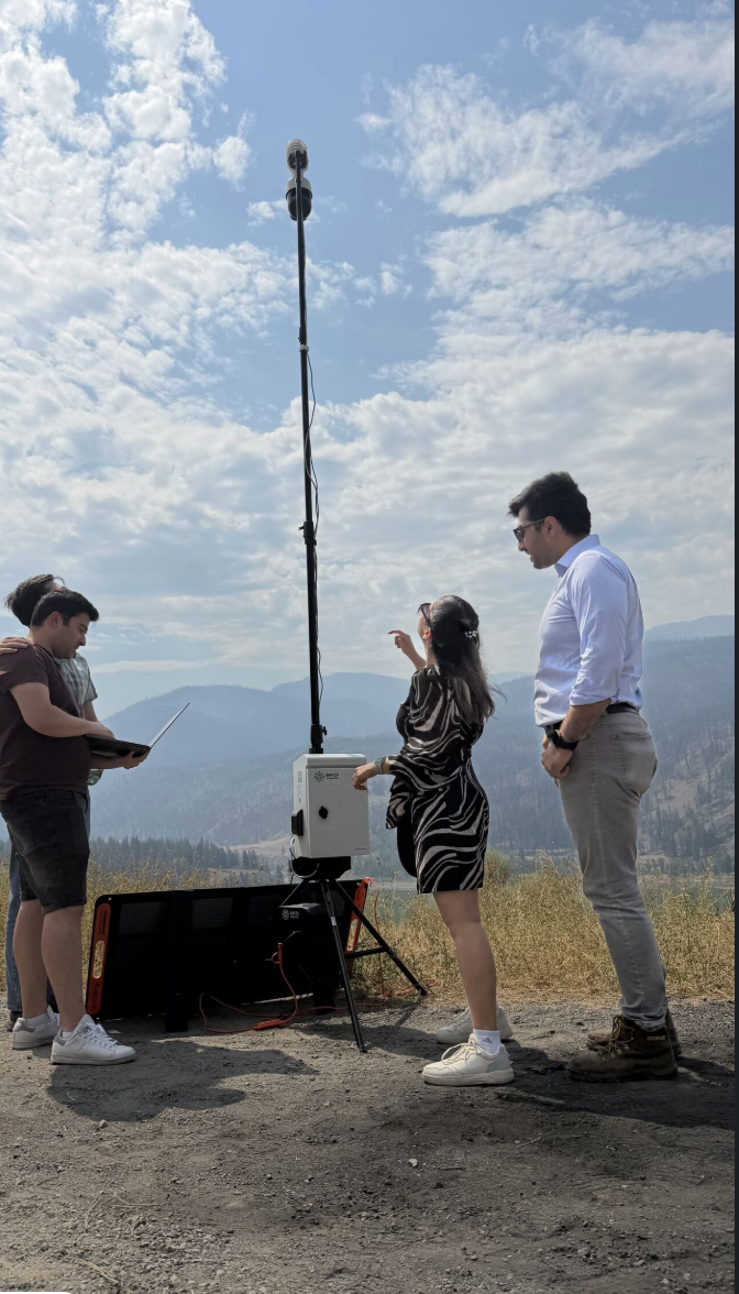 The Bayes Studio team stands on a hillside in Interior British Columbia, demonstrating their stationary multimodal monitoring unit.