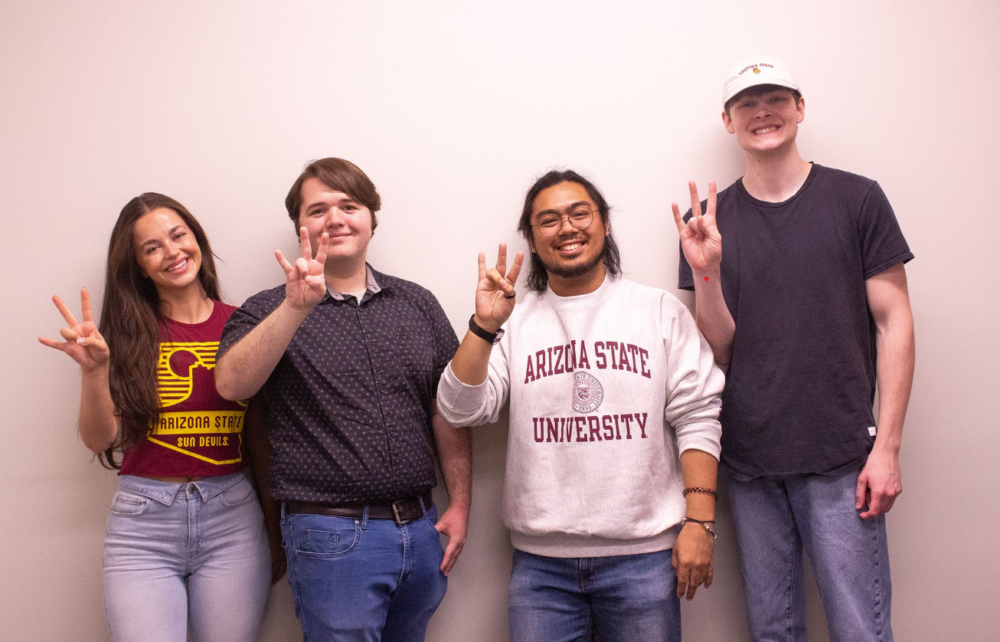 ASU SCAI capstone student engineers Emma Olivier, Matthew Tyson, Christian Izeck Ilog, and Zeb Moffat smiling and displaying the Arizona State pitchfork hand sign in front of a neutral backdrop.