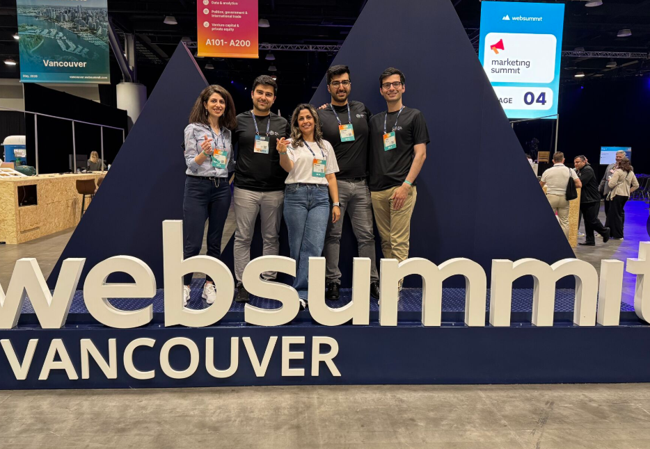Five Bayes Studio team members smiling and posing together in front of a large blue and white Web Summit Vancouver stage sign at the Vancouver Convention Centre.